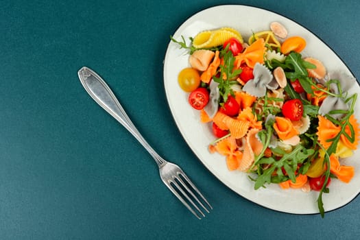 Salad with fresh tomatoes, herbs and pasta on a plate. Top view with copy space.