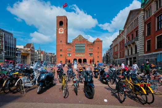 Amsterdam, Netherlands - May 7, 2017: Beursplein with parked bicycles and motorcycles and Beurs van Berlage building - former commodity exchange building now venue for concerts exhibitions conferences