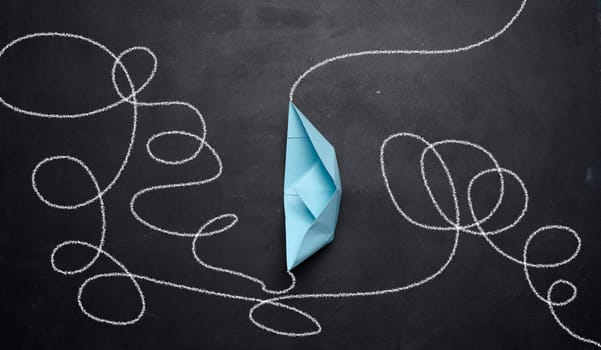 A blue paper boat and a tangled trajectory drawn in chalk. The concept of difficult decisions, a long way and overcoming difficulties