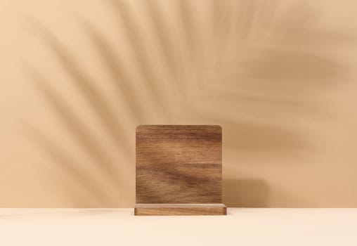 Wooden platform, shadow from a palm leaf on a brown background. Place for displaying cosmetics