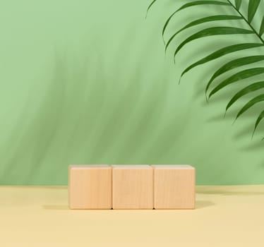 Platform made of wooden cubes and a palm branch on a green background, scenes for demonstrating and advertising products