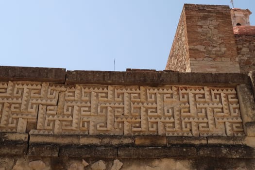 Ornamented ancient Zapotec wall next to the bell tower of the church of San Pablo Villa de Mitla at the archeological site of Mitla, Oaxaca, Mexico 2022