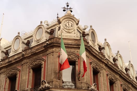 The top of building Edificio La Esmeralda with mexican flags, a clock, and many details and ornaments, Mexico City 2022