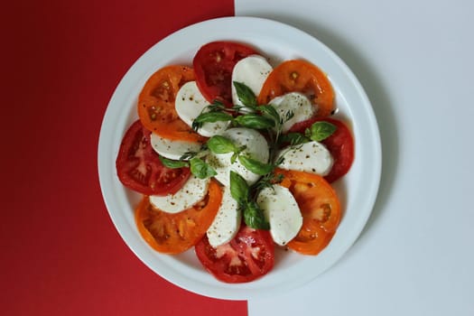 On a white plate is a tomato salad and decorated with white cheese on a red background