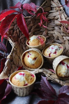 Fresh cupcakes with cherry filling are placed in a wicker basket and decorated with autumn leaves