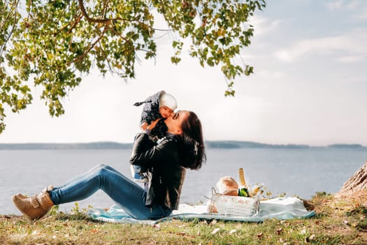 A dark-haired girl in sunglasses is relaxing with a baby on a picnic against the background of the sea