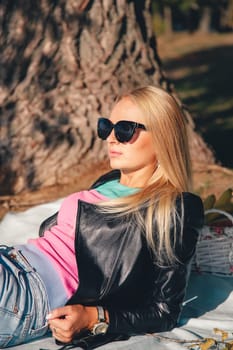 Blonde girl in sunglasses on a picnic near a tree in the park