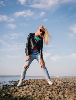 Blonde girl posing in ripped jeans in the afternoon on the shore of the blue sea