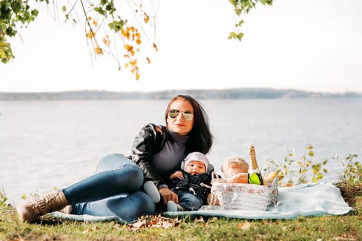 A dark-haired girl in sunglasses is relaxing with a child on a picnic against the background of the sea
