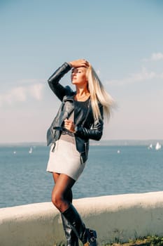A blonde girl with long hair and glasses poses on the shore of the blue sea in the afternoon
