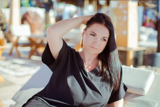 A brunette woman in a black dress is relaxing in a tent on the beach