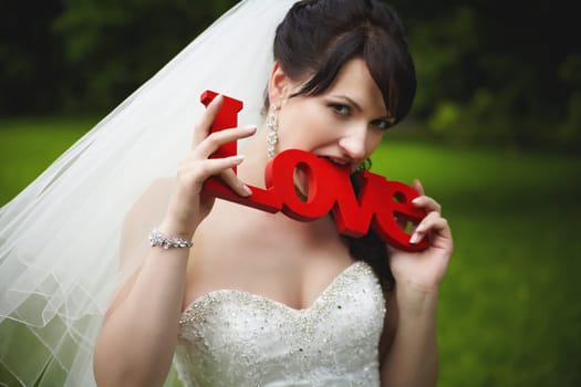 Cheerful bride bites wooden letters with the word love in red