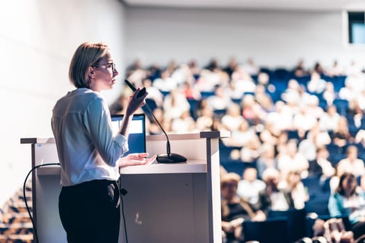 Female speaker giving a talk on corporate business conference. Unrecognizable people in audience at conference hall. Business and Entrepreneurship event