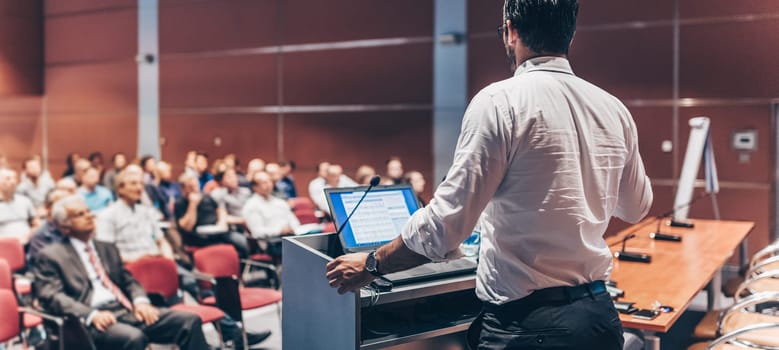 Speaker giving a talk on corporate Business Conference. Audience at the conference hall. Business and Entrepreneurship event. Panoramic composition.