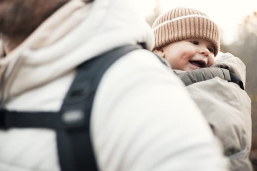 Sporty father carrying his infant son wearing winter jumpsuit and cap in backpack carrier hiking in autumn forest