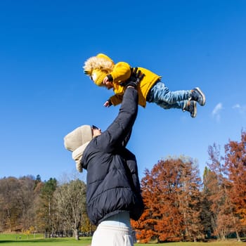 More, more,...mum, that's fun. Happy young mother throws her cute little baby boy up in the air. Mother's Day, Mather and her son baby boy playing and hugging outdoors in nature in fall