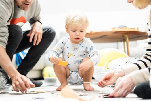 Parents playing games with child. Little toddler doing puzzle. Infant baby boy learns to solve problems and develops cognitive skills. Child development concept.