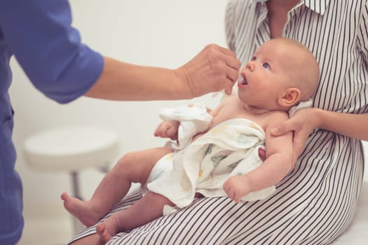 Pediatrician administring oral vaccination against rotavirus infection to little baby in presence of his mother. Children health care and disease prevention.