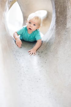 Child playing on outdoor playground. Toddler plays on school or kindergarten yard. Active kid on stone sculpured slide. Healthy summer activity for children. Little boy climbing outdoors