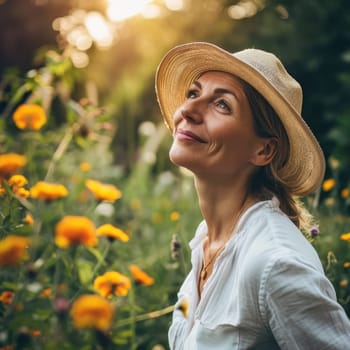 Portrait of a happy middle-aged woman wearing a straw hat outside in a graden with floers