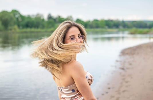 happy young woman with tousled hairs standing on riverbank