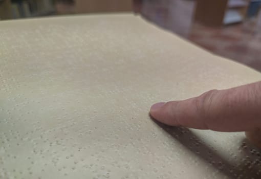 Blind male reading braille language book at library. Selective focus