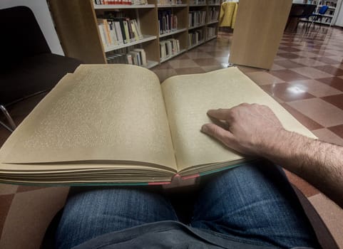 Blind male reading braille language book at library. Point of view shot