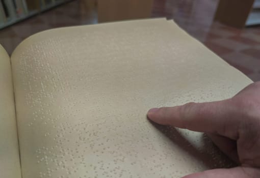 Blind male reading braille language book at library. Selective focus