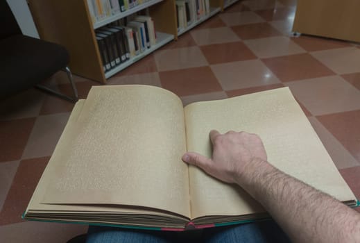 Blind male reading braille language book at library. Point of view shot