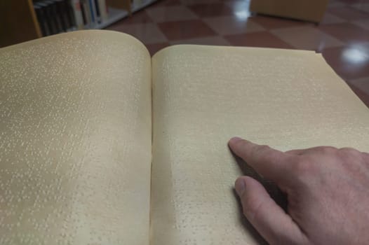 Blind male reading braille language book at library. Selective focus