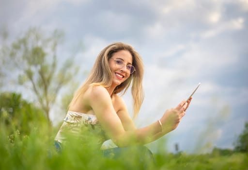 happy young woman with digital tablet sitting on a meadow