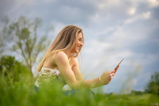 happy young woman with digital tablet sitting on a meadow