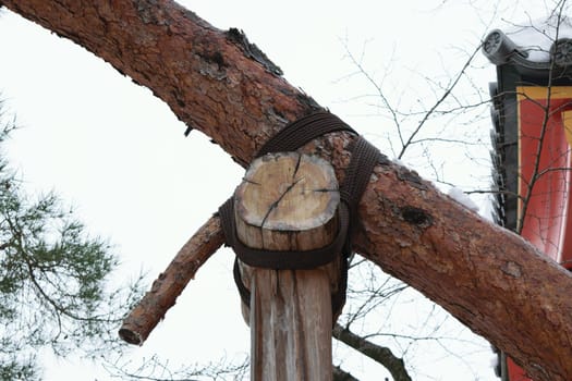 Traditional Japanese wooden pole to support a branch, against a backdrop of pine trees and a temple roof, symbolizing village guardians.