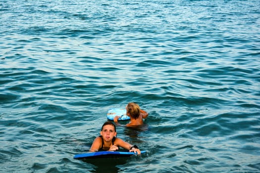 Two children with a swimming board in the sea water, girl cheekily sticks out her tongue