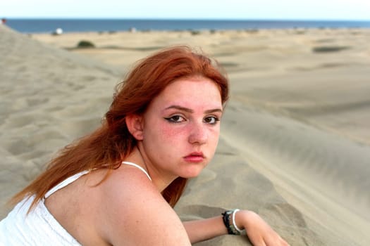 A young girl lies in the sand dunes in a white dress