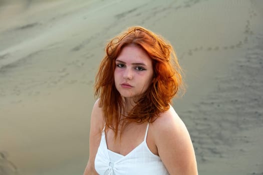Young girl with red hair, on the beach in summer, her hair tousled by the wind, and slight sunburn on the face