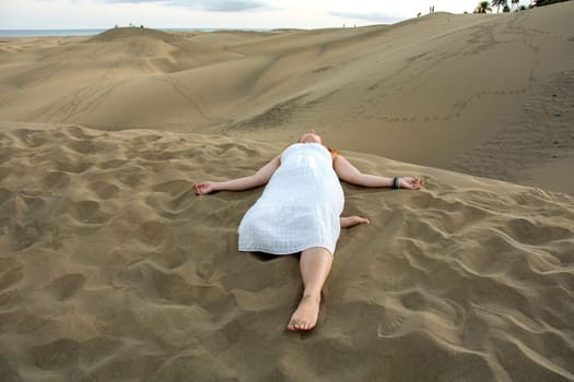 A young girl lies in the sand dunes in a white dress