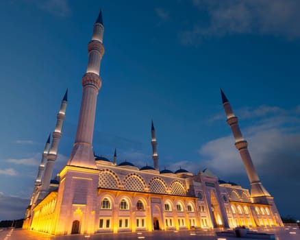 Camlica Mosque or Buyuk Camlica Camii, in Uskudar district, Istanbul, Turkey, lit up at night against blue sky. The minarets and domes are bathed in golden light, creating a magical scene