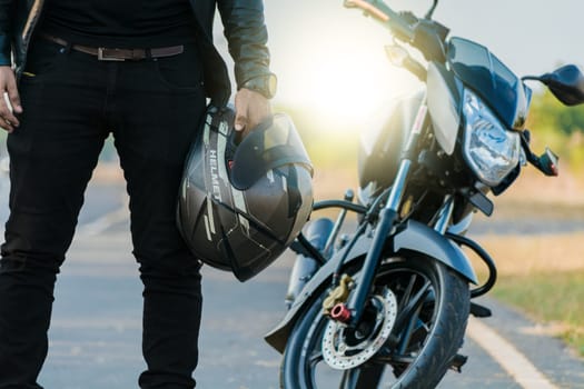 Unrecognizable biker holding helmet next to motorbike near the road. Motorcyclist holding safety helmet next to his motorbike near the road. Motorcycle safety helmet concept