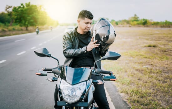 Young motorcyclist man putting on safety helmet outdoors. Male biker on motorcycle putting on helmet. Biker motorcycle safety concept