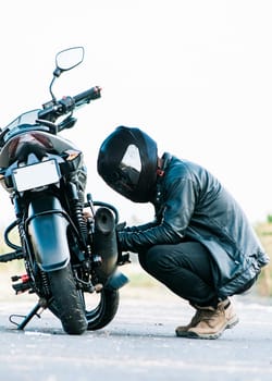 Man checking his motorcycle on the road. Motocyclist fixing the motorcycle on the road, Biker repairing motorcycle on the road