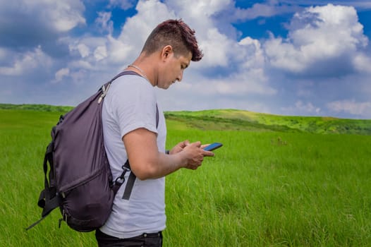 Man calling by cell phone, young man in the field calling by cell phone, young backpacker with cell phone in the field and copy space