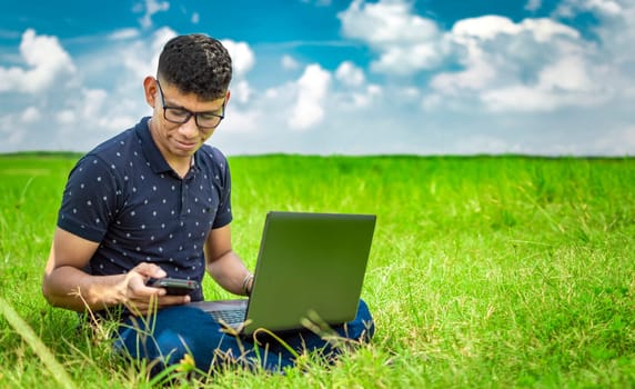 Young man in glasses working on his laptop, man in the field with his computer