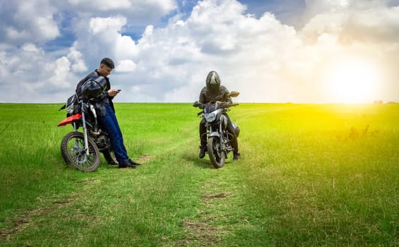 Two men with their motorcycles parked chatting in the field, two young motorcyclists in the field, two men on motorcycles on a beautiful country road, young motorcyclists parked on a road