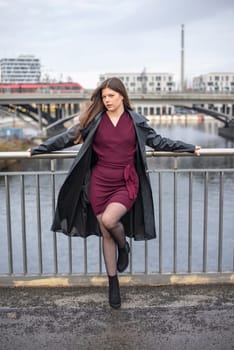 relaxed young woman wearing a black coat standing on a bridge