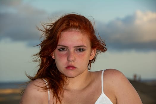 Young girl with red hair, on the beach in summer, her hair tousled by the wind, and slight sunburn on the face