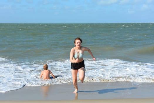 Two children have fun in the waves on the sea beach, Girl runs out of the water, boy sits in the waves