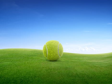 Tennis ball on green meadow on small hill and blue sky with clouds