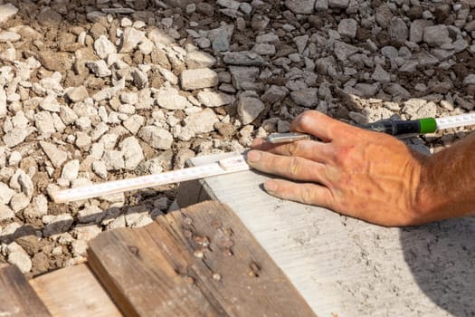 Drawing a straight line with a pencil on a concrete curb. Marking guidelines for cutting. Hands of a worker man.