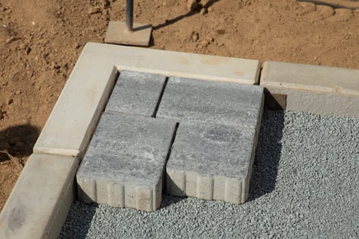 A gloved craftsman lays down the paving stones in layers. Laying gray concrete paving slabs in the courtyard of the house on a sandy foundation.